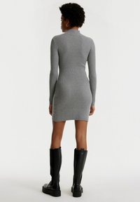 Graues, geripptes langärmliges Kleid mit einer figurbetonten Silhouette, in mittlerer Oberschenkel-Länge und hohem Kragen, kombiniert mit schwarzen kniehohen Stiefeln.