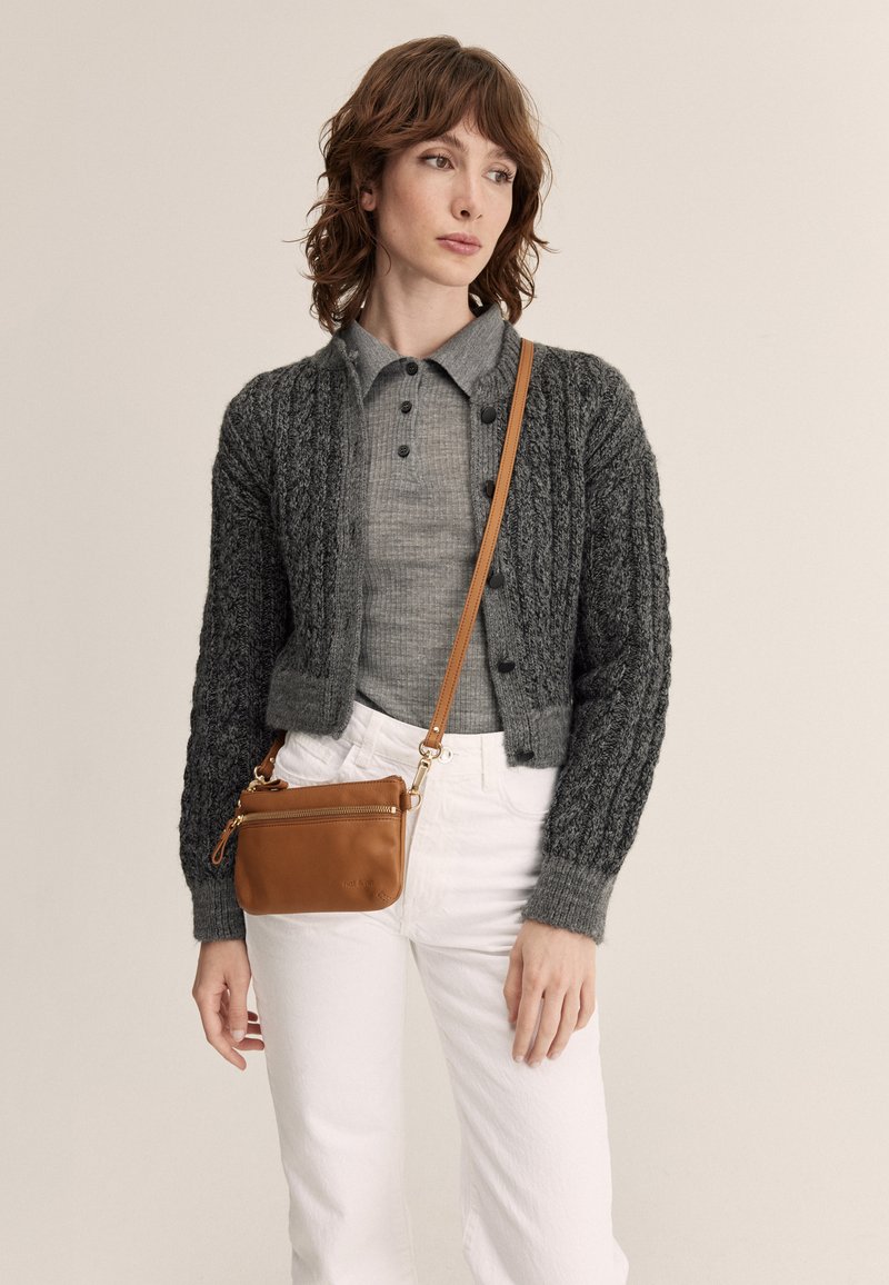 Gray knitted cardigan with textured patterns, gray polo underneath, white pants, and a tan leather crossbody bag with a zipper.