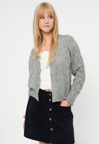 Grå strikket cardigan med diamantmønster, ribbede mansjetter og fem knapper. Kombinert med en mørk kordfløyelskjørt med store lommer.