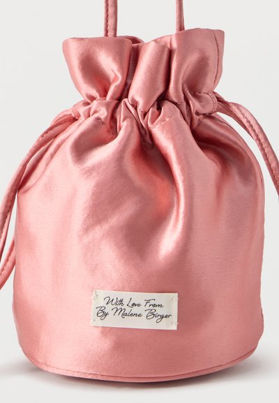Πουγκί από σατέν με κορδόνι σε απαλό ροζ χρώμα, με κορυφή που μαζεύει και λευκή ετικέτα που γράφει "Με αγάπη από By Malene Birger."