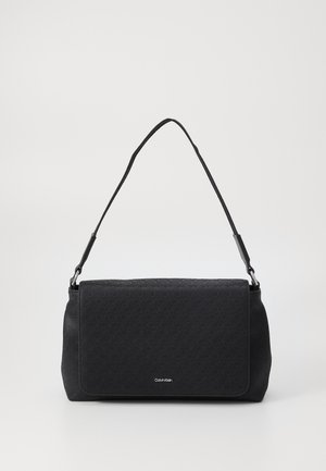 Sac à bandoulière noir Calvin Klein avec fermeture à rabat, motif de logo subtil et bandoulière réglable sur un fond uni.