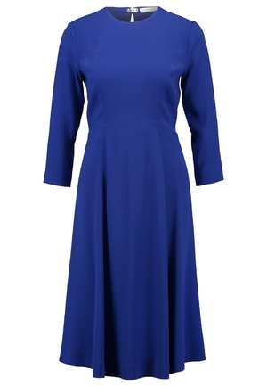 Kuningas sininen mekko, jossa on pyöreä kaula-aukko, kolme neljännesosaa hihat ja levenevä helma, yhdistettynä mustiin ja valkoisiin korkokenkiin.