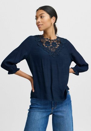 Marinebluse mit floralen Spitzenverzierungen am Ausschnitt, dreiviertel Ärmel mit elastischen Bündchen und leichtem strukturiertem Stoff.