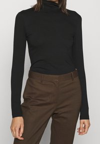 Svart långärmad polotröja i stretchigt material. Matchas med bruna skräddarsydda byxor med slät yta och figursydd design.