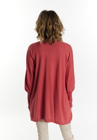 Dlhý rukáv cardigan v koralovej farbe, s voľným strihom, rebrovanými manžetami a zaobleným lemom. Mäkká tkanina s hladkou textúrou.
