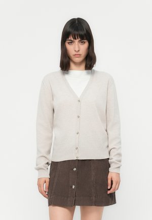 Beige cardigan with a v-neck, button-down front, and long sleeves, made from soft fabric. Paired with a brown corduroy skirt featuring buttons.