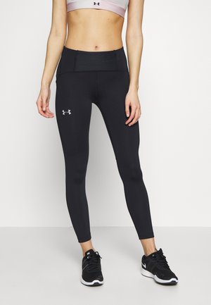 Frau trägt schwarze Under Armour Leggings, pinken Sport-BH und schwarze Nike Laufschuhe, steht vor einem weißen Hintergrund.
