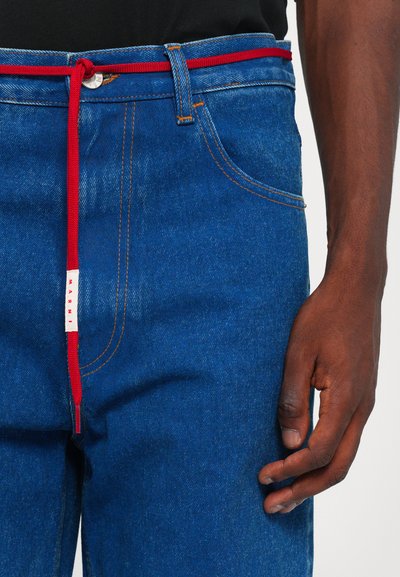 Jeans de mezclilla azul con un cinturón de cuerda rojo, con costuras naranjas y una pequeña etiqueta blanca con "MARNI" en la cinturilla delantera.