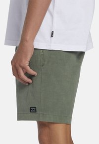 Groene linnen shorts met een ontspannen pasvorm, voorzien van een zwart logo op de zoom, en gecombineerd met een plain wit T-shirt.