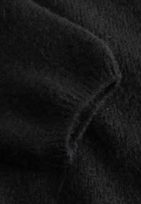 Čierna pletená látka s jemnou, chlpatou textúrou, vybavená rebrovanými okrajmi a mierne voľným vzorom tkania, ktorá pôsobí útulne.