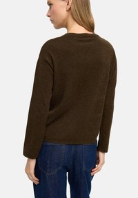 Brązowy sweter z dzianiny z okrągłym dekoltem i długimi rękawami, charakteryzujący się luźnym krojem i miękką teksturą. W połączeniu z niebieskimi dżinsami.