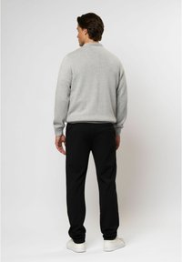 Pilkas mezginys megztinis su aukšta apykakle, juodos siaurėjančios kelnės ir baltos sportinės bateliai. Lygus paviršius, laisvas siluetas ir minimalus dekoras.