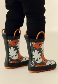 Bottes de pluie en caoutchouc noires avec un design coloré d'Halloween représentant des momies, des citrouilles et des fantômes. Accents orange et semelles texturées.