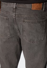 Szare dżinsy z denimu o lekko wyblakłej fakturze, z dwoma tylnymi kieszeniami i skórzaną metką na pasku od spodni.