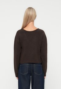 Pull en bronze, court, avec un col rond et des épaules tombantes. Texture douce associée à un jean en denim bleu foncé visible en dessous.