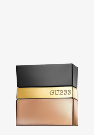 Flacon de parfum rectangulaire avec bouchon noir, bande centrale dorée gravée "GUESS" et base en verre brun clair givré.
