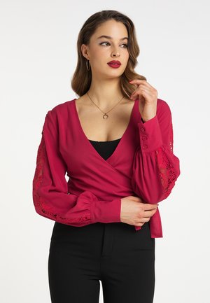 Fuchsiový zavinovací top má dlouhé puff rukávy s krajkovými detaily, hluboký V-výstřih a knoflíky na manžetách, spárovaný s černými kalhotami.