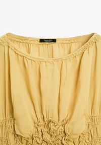 Gelbe, strukturierte Bluse aus leichtem Stoff. Verfügt über eine geraffte Detailverarbeitung am Ausschnitt und Saum, mit einem Etikett von Massimo Dutti.