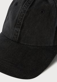 Casquette de baseball en coton noir avec une visière courbée et des détails de couture visibles, présentée sur un fond blanc uni.