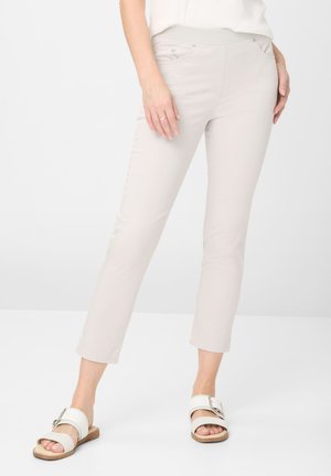 Lys beige cropped bukser med en glat overflade, udstyret med en flad talje og sidelommer, parret med hvide sandaler på en hvid baggrund.