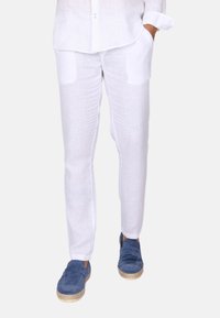 Bílé lněné kalhoty z lehké, strukturované látky. Mají boční kapsy a přiléhavý střih. Spárované s modrými espadrilkami.