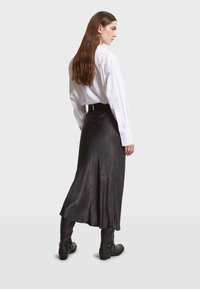 Jupe en cuir noir mi-longue avec une texture lisse, dotée d'un ourlet évasé et associée à des bottes noires ajustées jusqu'au genou et une chemise blanche.