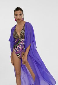 Kimono trasparente viola sopra un costume da bagno a stampa leopardo con motivi astratti multicolori. Il tessuto è leggero con maniche ampie.