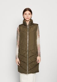 Gilet matelassé vert olive avec col haut, doté d'une fermeture éclair frontale, d'un motif de matelassage en chevrons et de poches latérales.