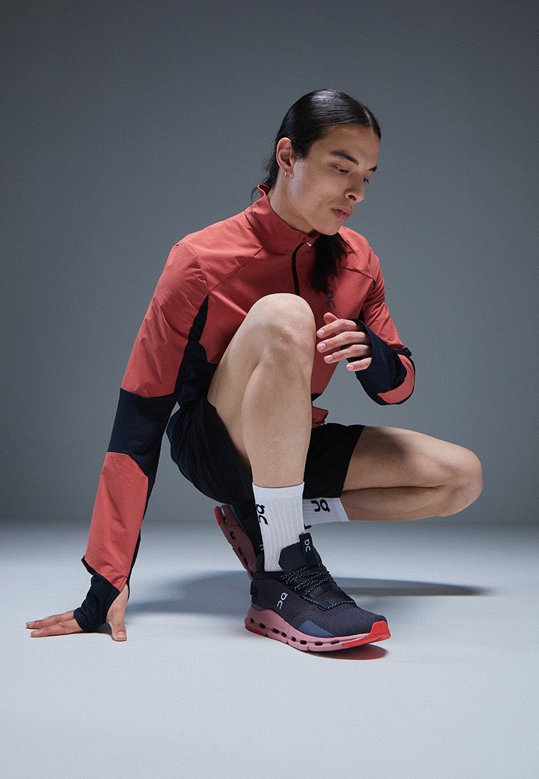 Atletische outfit met een rood en marineblauw zip-top, zwarte shorts en zwarte hardloopschoenen met rode accenten en een uniek zoolontwerp.