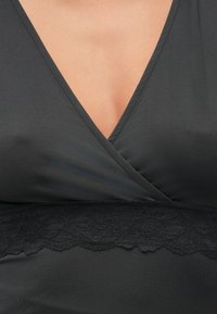 Close-up van een persoon die een zwart V-hals kledingstuk draagt met een kantbanddetail onder de borst.