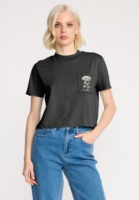 Czarny, skrócony t-shirt z miękkiego materiału, z jedną kieszonką z przodu ozdobioną kwiatowym wzorem w kolorze białym oraz małym logo nad kieszonką.