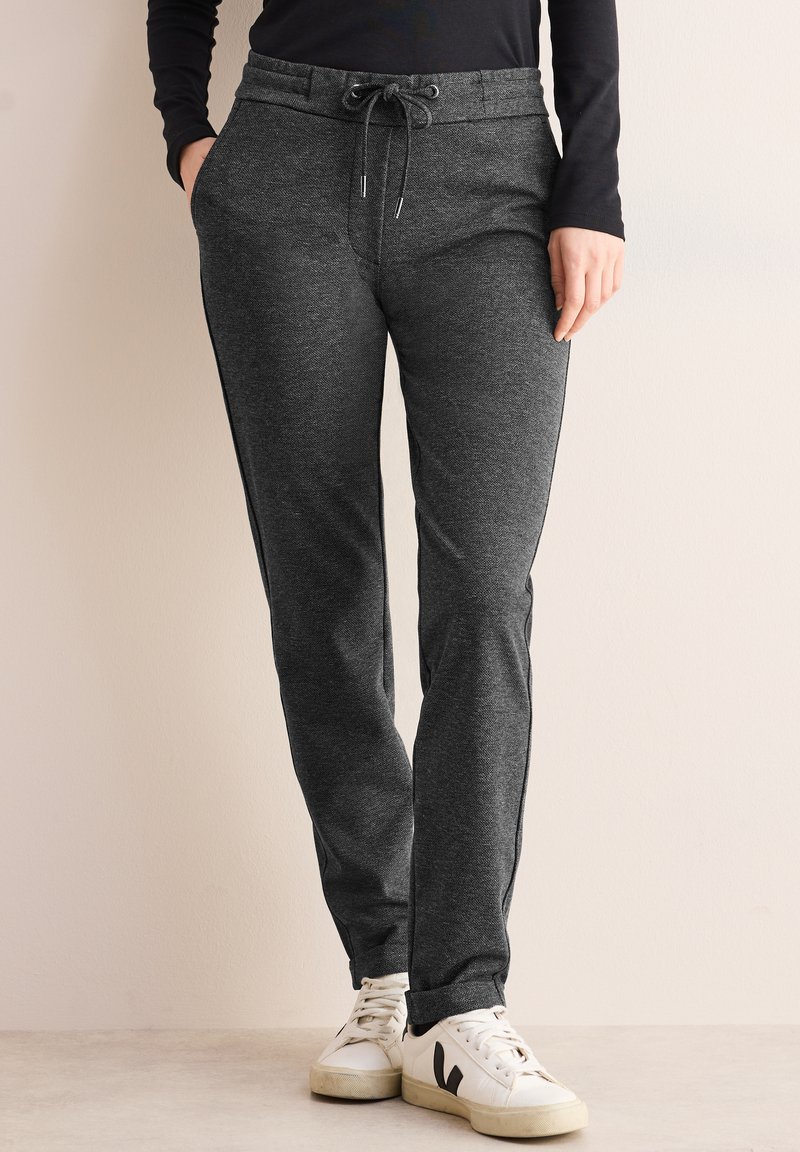 Un survêtement gris avec une taille à cordon de serrage, des jambes fuselées et des poches latérales. Associé à des baskets blanches avec des accents noirs.