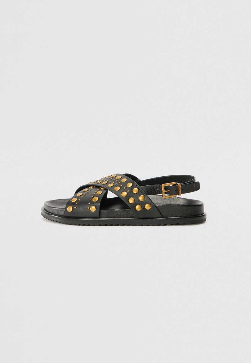 Black leather sandals featuring cross straps adorned with gold studs and a buckle closure. Soft sole with textured grip for traction.