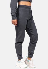 Dunkelgraue Jogginghose aus weichem Stoff, mit einem Kordelzugbund, seitlichen Taschen und elastischen Bündchen. Kombiniert mit weißen Sneakers.