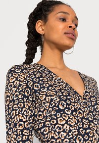 Blusa de decote em V com padrão de leopardo, feita de tecido macio, apresentando um fundo azul-marinho com manchas em creme e cor de ferrugem e mangas longas.