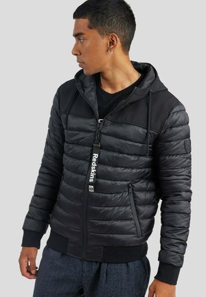 Doudoune noire avec un design matelassé horizontal, fermeture zippée, capuche et poignets côtelés. Comprend un zip avec tirette de marque et des poches latérales.
