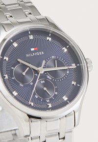 Montre en acier inoxydable argenté avec un cadran texturé bleu marine, trois sous-cadrans, index horaires argentés et logo de la marque affiché. Bracelet en maillons métalliques.