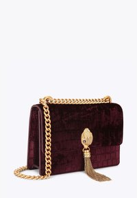 Bordowa aksamitna torebka o fakturze krokodyla, z złotym łańcuszkiem jako paskiem i dekoracyjnym złotym zapięciem w kształcie ręki z chwostem na przedniej klapie.