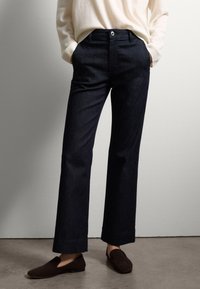 Pantalones de mezclilla azul oscuro con corte recto, que cuentan con bolsillos delanteros, un cierre de un solo botón y bordes doblados. Textura suave.