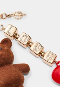 Goldfarbener Anhänger mit einem braunen Teddybär, kubischen Buchstaben, die "LIEBE" buchstabieren, mit Strassakzenten, und einem roten herzförmigen Anhänger.