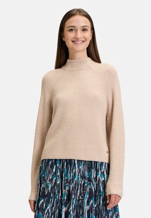 Light beige ribbed sweater with a high neck and long sleeves, paired with a pleated blue and green patterned skirt.