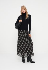 Suéter de cuello alto negro combinado con una falda maxi de rayas blancas y negras que fluye. La modelo lleva un bolso negro de hombro y botas negras de tacón.