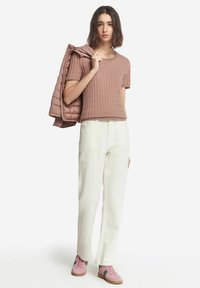 Kortärmad, texturerad rosa topp med ribbing, matchad med vita byxor och rosa sneakers med gröna detaljer. Jacka hängande över axeln.