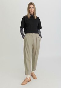 Zwart t-shirt met korte mouwen over een marineblauw en wit gestreept overhemd met lange mouwen, gecombineerd met lichtbeige geplooide broeken en bruine instappers.