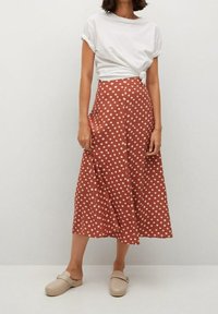 Terrakotowa midi spódnica w białe kropki, wysoki stan, lekki materiał, zestawiona z białym t-shirtem z węzłem i beżowymi klapkami.
