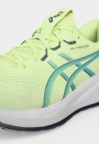 Νεον κίτρινο παπούτσι τρεξίματος Asics Gel-Cumulus 28 με μπλε ρίγες, άσπρη μαλακή σόλα και αεριζόμενο πλέγμα στο επάνω μέρος με κορδόνια.