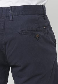 Marineblaue Shorts aus strukturiertem Material, mit flachem Vorderteil, Seitentaschen und einer geknöpften Gesäßtasche mit Markenakzenten.