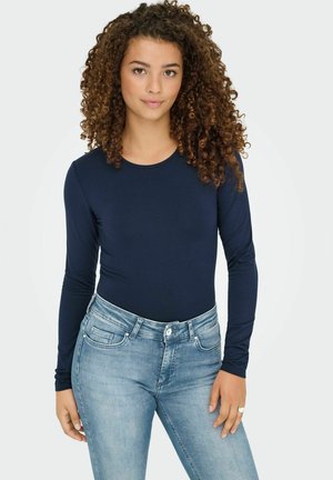 Marineblå langærmet bodysuit lavet af blødt stof, med rund hals og tætsiddende design, parret med lyseblå denimjeans.