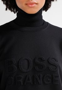 Svart polotröja med strukturerad broderad "BOSS ORANGE"-text som tydligt visas på framsidan. Mjuk textil med ribbad struktur.