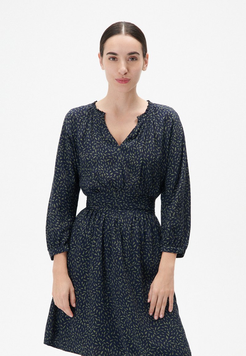 Marineblaues Kleid mit Taillierung und weitem Rock. Es verfügt über einen V-Ausschnitt und lange Ärmel, verziert mit einem grünen, verstreuten Muster.